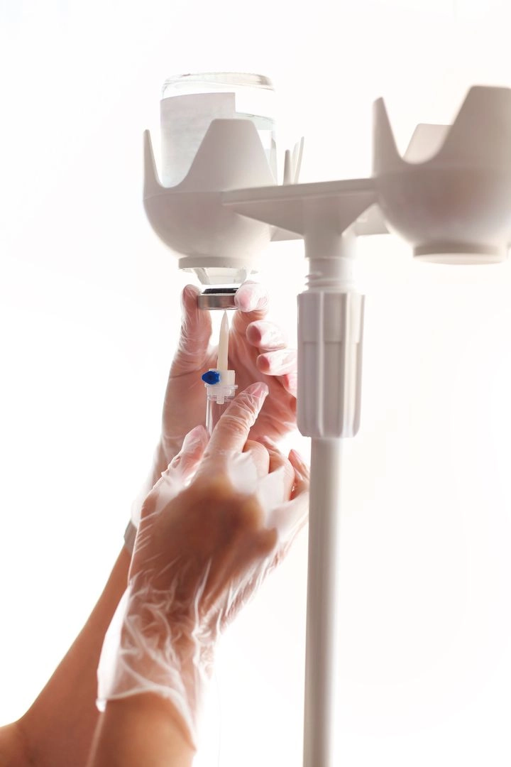 Manos con guantes preparando un equipo de infusión, dispositivo médico
