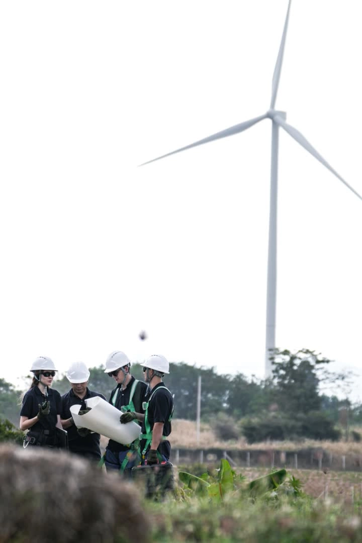 Técnicos con casco revisando planos junto a un aerogenerador